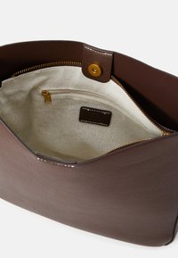 Intérieur d'un sac en cuir marron avec un revêtement en tissu beige. Comprend une poche zippée, du matériel doré et une fermeture à pression sur le dessus.
