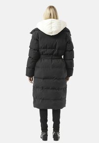 Schwarzer Steppmantel mit weißem, gesteppter Kapuze, tailliertem Gürtel und strukturierten Partien. Der Mantel ist lang, hat eine lockere Passform und verdeckte Taschen.