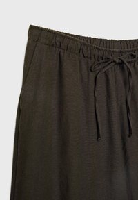 Pantalon noir à cordon de serrage avec taille élastique et poches latérales sur un fond clair.