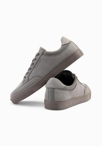 Šedé semišové tenisky s nízkým designem, kulatou špičkou a šněrováním. Mají texturovanou gumovou podrážku a decentní logo.