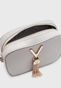 Borsa in ecopelle grigia con texture, dotata di hardware dorato, caratterizzata da un accento a forma di V e una nappina a catena, chiusura zip sulla parte superiore.