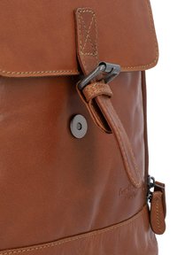 Zaino in pelle marrone con chiusura a pattina, fibbia in metallo e bottone a scatto. Presenta cuciture a contrasto e una tasca laterale con zip.