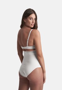 Shapewear bianco a vita alta con spalline regolabili e chiusura a gancio sul retro, realizzato in un tessuto liscio ed elasticizzato con cuciture minime.