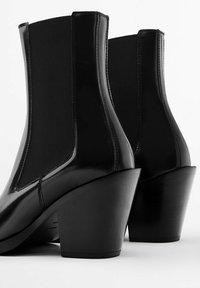 Black ankle boots featuring glossy leather, elastic side panels, and a chunky high heel for stability. Smooth texture with a sleek design.