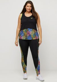 Zwarte sportieve tanktop met een multicolore bloemenprint onderlaag, gecombineerd met zwarte tights met kleurrijke zijaccenten en neonafwerking.