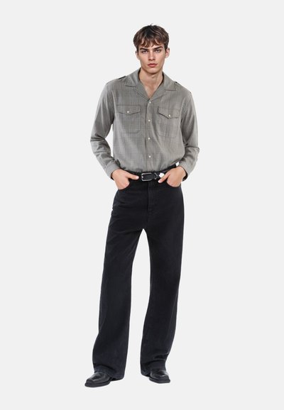 Grå ternet skjorte med lange ærmer og to brystlommer, parret med sorte fløjl bukser. Et sort bælte og fodtøj fuldender outfittet.