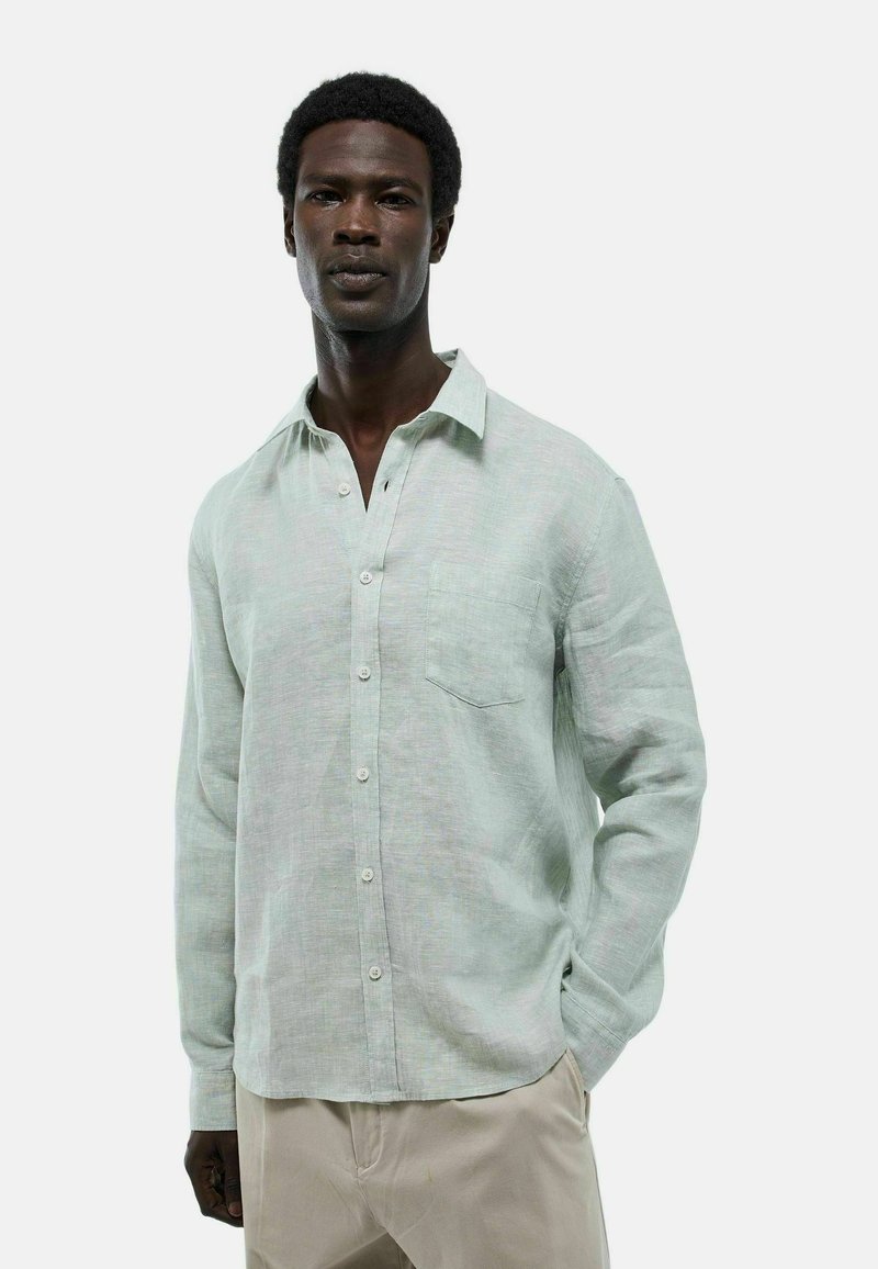 Chemise en lin vert clair avec col boutonné, poche frontale et manches longues. Tissu texturé avec une coupe décontractée.