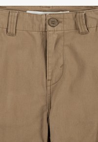 Pantalones caquis con cierre de botón, frente plano y bolsillos laterales. Fabricados en un tejido suave con costuras visibles.