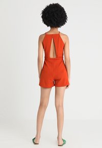 Rode polyester jumpsuit met een sleutelgat achter, aansluitend lijfje en losse shorts. Heeft dunne bandjes en een cinched taille.