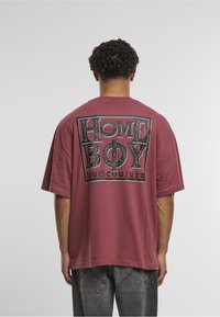 Bordové oversize tričko z bavlny, s černým grafickým potiskem na zádech s nápisem "HOME BOY loud.couture". Krátké rukávy.