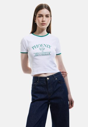 Camiseta corta blanca con detalles en verde, que presenta el texto "CLUB DE TENIS PHOENIX". Combinada con jeans de mezclilla azul oscuro de cintura alta.