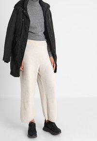 Czarna pikowana kurtka na szarym swetrze z golfem, zestawiona z kremowymi spodniami o szerokich nogawkach i czarnymi sneakersami, prezentuj�ąca miękkie faktury i luźny krój.