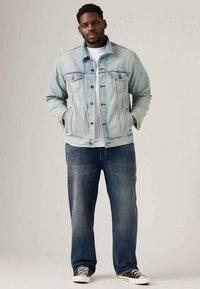 Lichtblauwe denimjack met borstzakken, knoopsluiting en een wit T-shirt eronder. Gecombineerd met donkerblauwe jeans en zwarte sneakers.