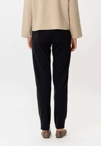 Čierne nohavice so slim fit strihom, vyrobené z mäkkej tkaniny. Modelka má na sebe hnedé baleríny; vrchný diel je béžový, so voľným strihom a dlhými rukávmi.