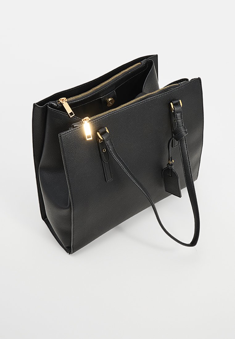 Borsa a tracolla in pelle nera con dettagli in oro sulla cerniera, forma strutturata, tasche interne e un'etichetta per bagagli staccabile.