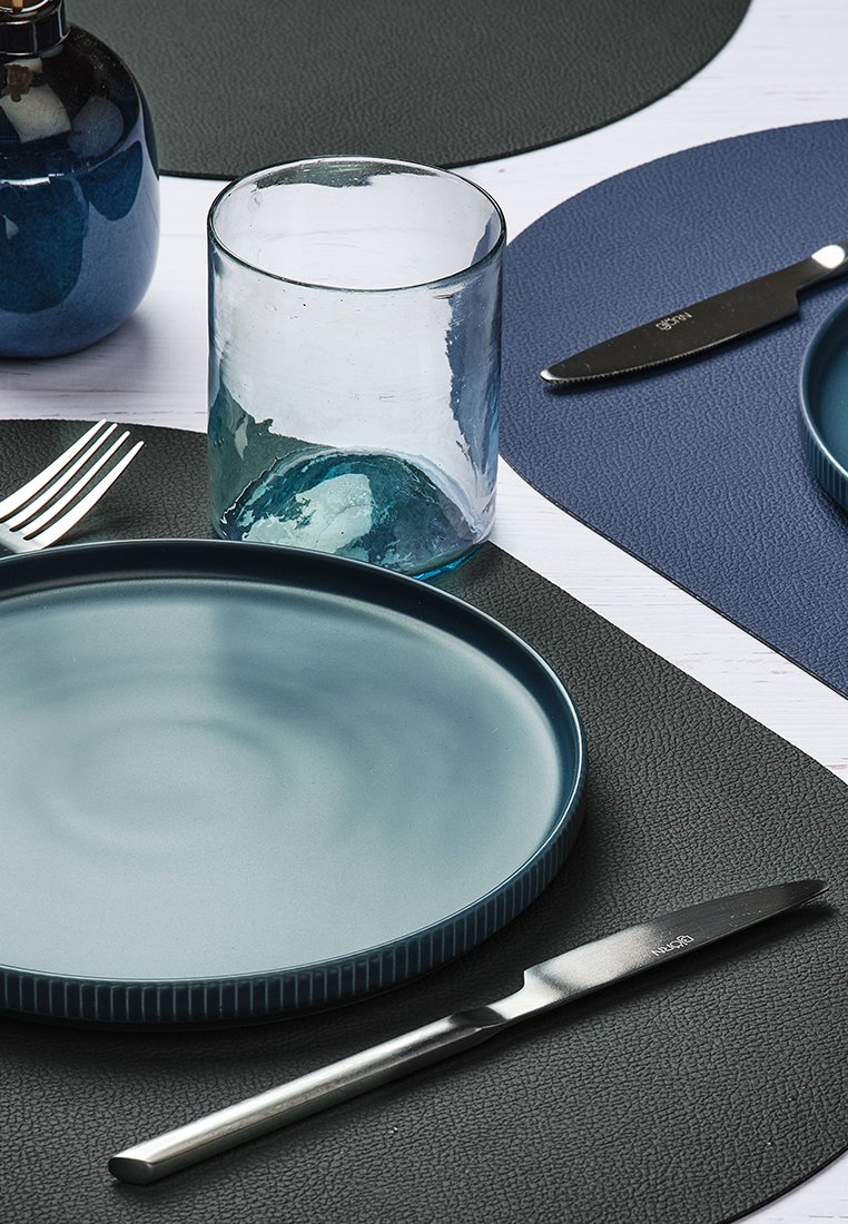 Keramikplatte, sanfter blauer Farbverlauf, gerippter Rand; klares Glas-Glas; Edelstahlmesser; strukturierte, dunkle Platzsets; dunkelblaue Akzentmatte.