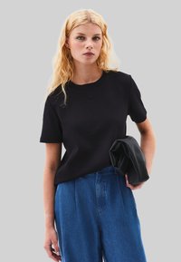 Sort bomulds t-shirt med korte ærmer og rund halsudskæring, parret med højtaljede blå denimbukser og en sort sammenfoldelig clutch.