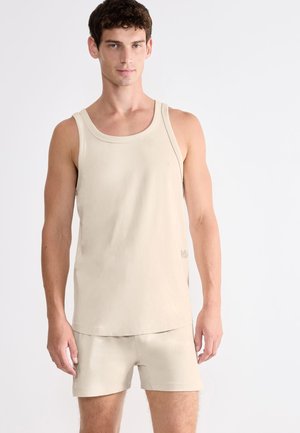 Beige Baumwoll-Tanktop mit rundem Ausschnitt, locker geschnitten und mit Steppnähten, kombiniert mit passenden Shorts in ähnlicher Farbe.