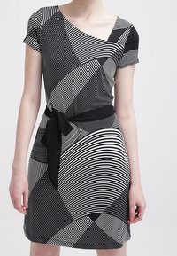 Svartvit mönstrad klänning med korta ärmar, asymmetrisk halsringning, midjeband, med ränder, prickar och olika geometriska former.