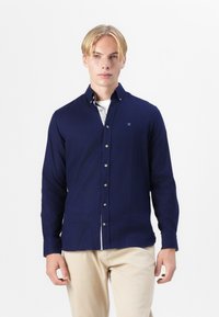 Camisa de botones azul marino de manga larga, con una textura sutil y botones en la parte delantera. Incluye un dobladillo de hem patrón.