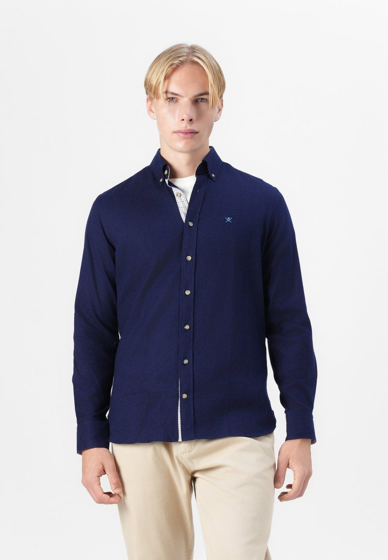Camisa de botones azul marino de manga larga, con una textura sutil y botones en la parte delantera. Incluye un dobladillo de hem patrón.