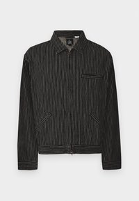 Chaquetón negro con rayas blancas verticales, cierre frontal de botones, cuello, mangas largas y dos bolsillos laterales. Incluye un bolsillo en el pecho.