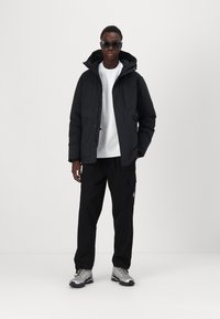 Sort pufferjakke med hætte, parret med en hvid sweatshirt og sorte cargo-bukser. Grå sneakers fuldender outfittet.