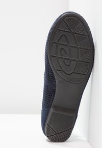 Semelle d'une chaussure bleu marine avec une semelle en caoutchouc texturée, taille 37, appuyée contre une surface blanche.
