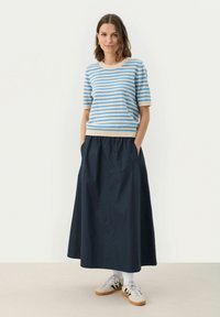 Randig blå och beige stickad topp med korta ärmar, i kombination med en högmidjad marinblå kjol. Modellen har vita strumpor och grå sneakers.