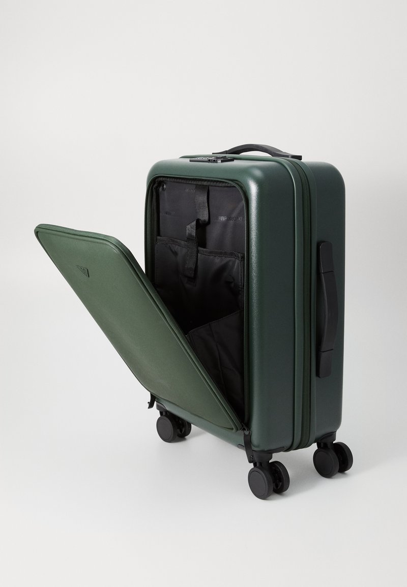 Maleta rígida de color verde oscuro, con apertura con cremallera y un interior negro con bolsillos organizadores. Cuatro ruedas negras para mayor movilidad.