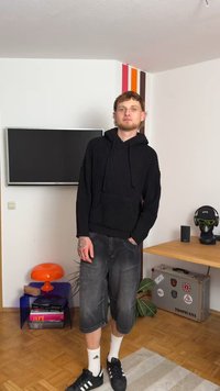 Must meistitud musträmpä, hallid vabaaja lühikesed püksid, mustad spordijalatsid ja valged sokid; minimaalsed aksessuaarid ja siseruum.