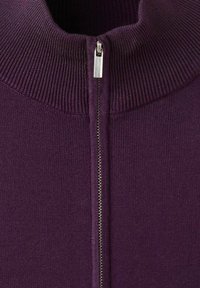 Primo piano di un maglione viola a maglia con collo alto a coste e una cerniera argentata parzialmente chiusa al centro davanti.