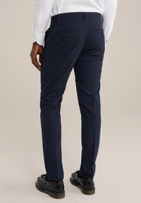 Pantalons à carreaux bleus marine avec une coupe ajustée, texture lisse, deux poches arrière avec bouton et petites fentes à l'ourlet, associés à des chaussures noires.