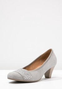 Chaussure à talon haut en daim gris avec un bout arrondi, présentant un détail en strass scintillant sur le bout et un talon carré texturé.