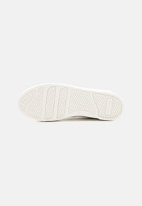 Suola di una sneaker, bianca con un motivo testurizzato, caratterizzata da scanalature orizzontali e un marchio. Finitura liscia con un design robusto per una buona presa.