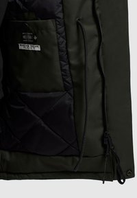 Grøn stofjakke med sort quiltet for, med sidelomme, lynlåslukning og justerbar kant med snøre.