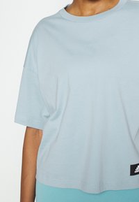 Osoba ve volném světle modrém krátkém tričku s logem Adidas na spodním lemu na pravé straně.
