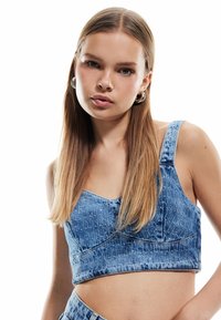 Top corto in denim di colore azzurro chiaro, con un motivo testurizzato e spalline larghe. Presenta un collo a cuore e dettagli di cucitura visibili.
