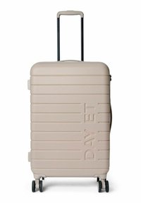 Valise rigide beige clair avec surface texturée, rainures horizontales, poignée rétractable et quatre roues pour faciliter la mobilité.