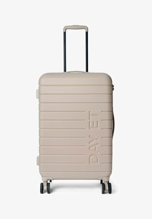 Valise rigide beige clair avec surface texturée, rainures horizontales, poignée rétractable et quatre roues pour faciliter la mobilité.