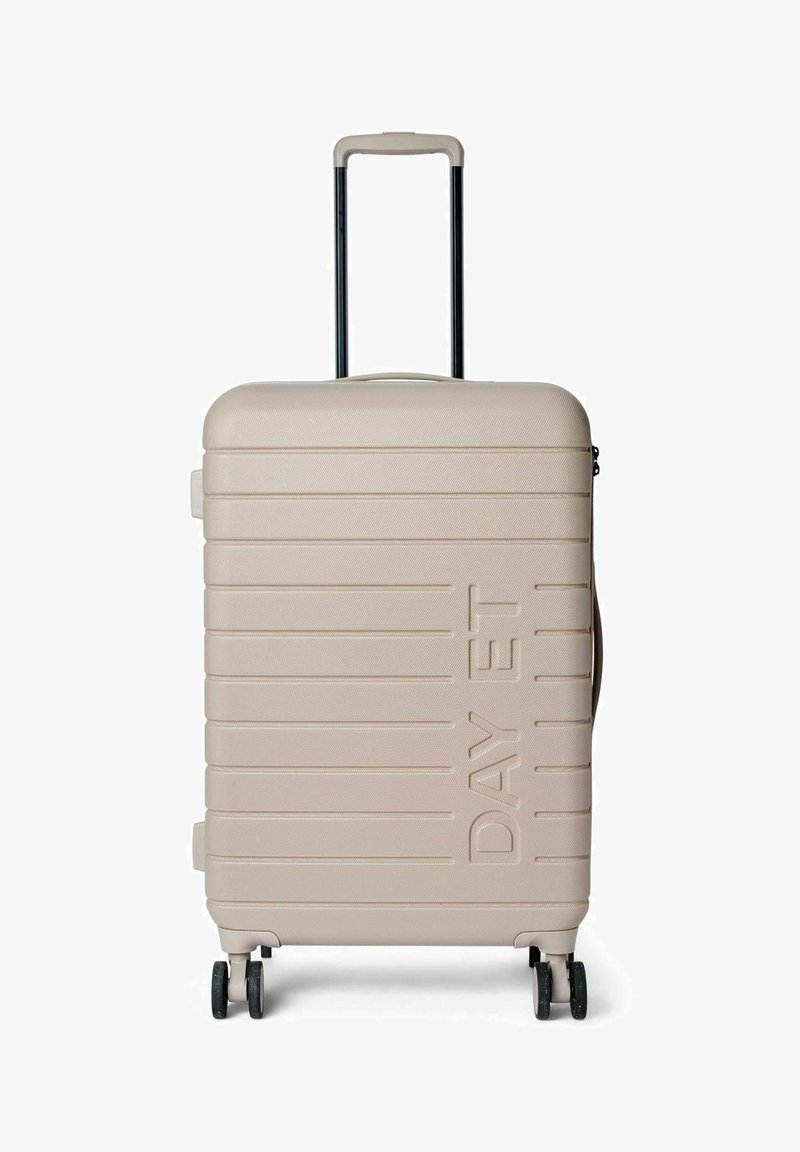 Valise rigide beige clair avec surface texturée, rainures horizontales, poignée rétractable et quatre roues pour faciliter la mobilité.