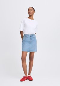 Denim A-line skirt in light blue, paired with a plain white T-shirt and red sneakers. Features a waistband with belt loops and front pockets.