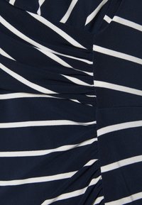 Tissu bleu marine avec des rayures blanches horizontales. Présente une texture froncée sur un côté, créant un effet superposé. Matériau doux et extensible.