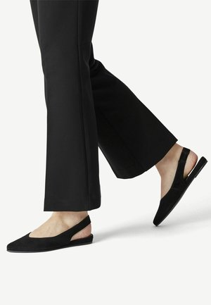 Sorte ruskinds slingback flade sko med spids tå, udskæringsdesign på siderne og flad sål, parret med sorte vide bukser.