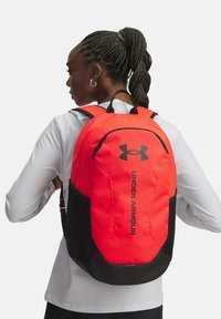 Punane ja must Under Armour seljakott, millel on vooluline disain, pehmed rihmad ja silmatorkav logo esiküljel. Vastupidav materjal.