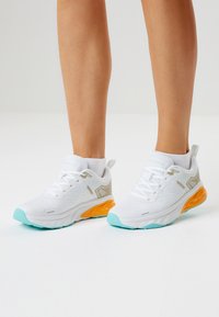 Valkoiset urheilukengät, joissa on teksturoitu päällinen, vaaleanharmaat yksityiskohdat sekä oranssi-petrolinsävyinen pohja. Nauhallinen malli ja pehmustettu varren reuna.