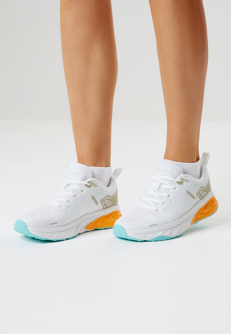 Valkoiset urheilukengät, joissa on teksturoitu päällinen, vaaleanharmaat yksityiskohdat sekä oranssi-petrolinsävyinen pohja. Nauhallinen malli ja pehmustettu varren reuna.