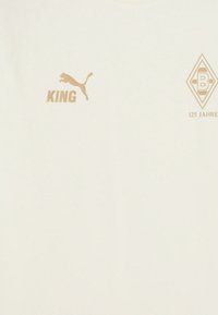 Cremefarvet t-shirt lavet af bomuld, prydet med guld logoer: "KING," en springende Puma-kat, og en diamantform med "125 JAHRE."