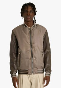 Giacca bomber marrone con tessuto liscio, collo e polsini a costine a righe, tasche con cerniera e chiusura con bottoni a pressione.