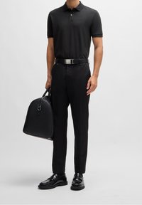 Svart pikétröja med korta ärmar, svarta byxor, glänsande svarta loafers och en strukturerad svart väska med rundad topp. Silverbuckle-detalj.